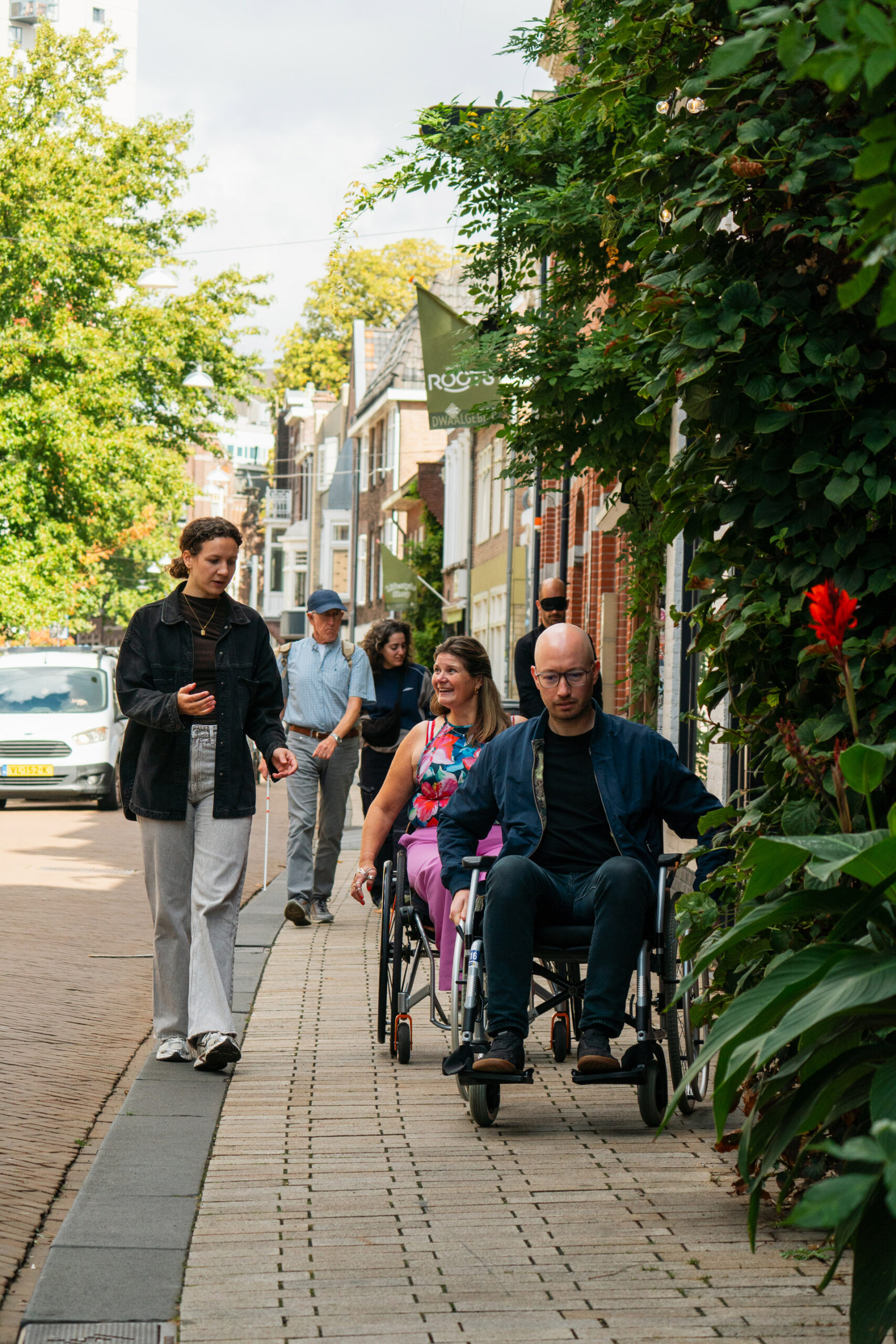Begaand: Medewerkers van Noeste IJver doen mee aan een workshop over toegankelijkheid in de stad. Een medewerker zit in een rolstoel en anderen lopen geblindoekt over de stoep.