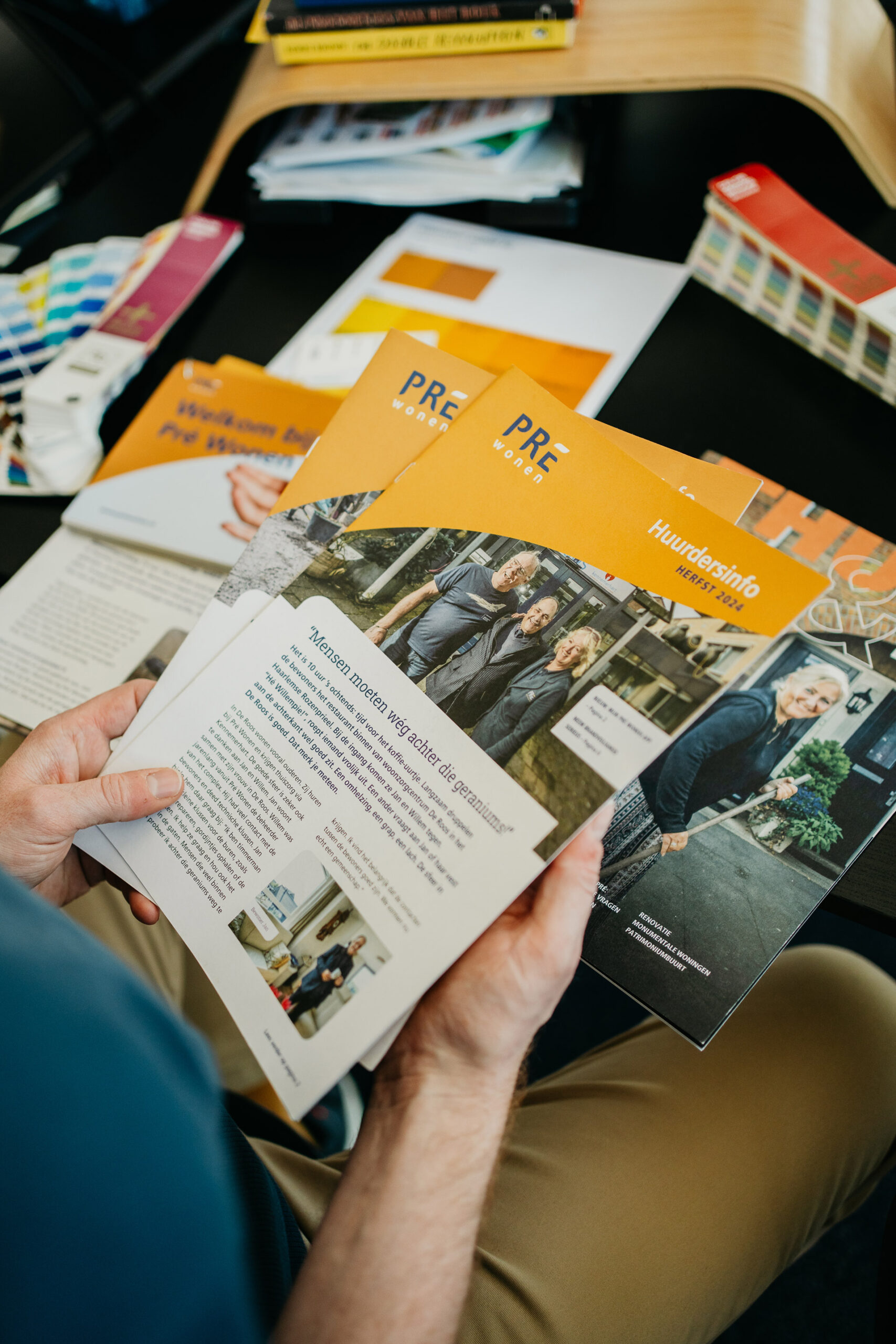 Merkwaardig: Een medewerker houdt drukwerk in zijn handen van een woningcorporatie. Op de achtergrond liggen diverse stukken drukwerk als een magazine, kaarten en grafische materialen.